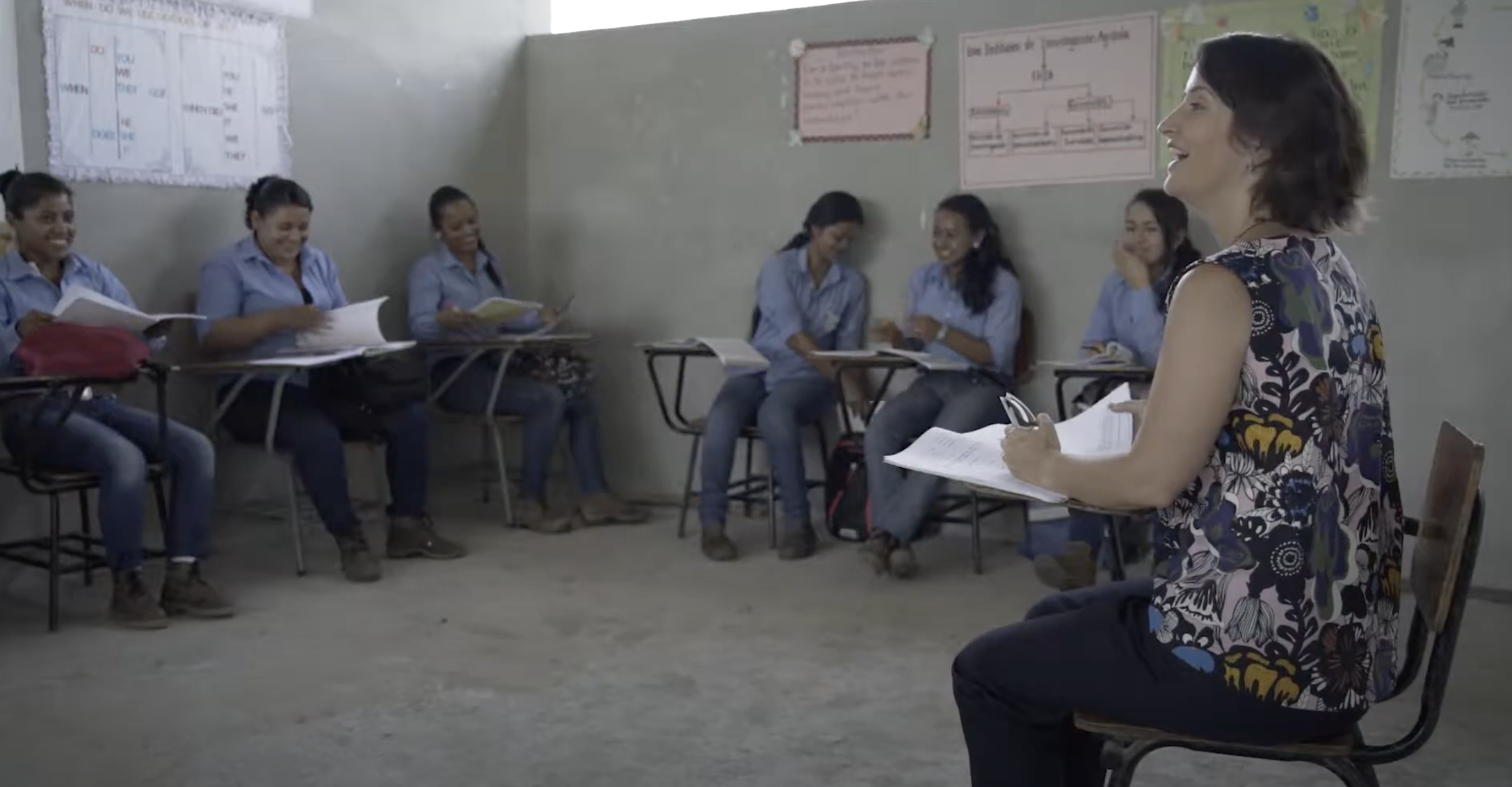 Dr. Erin Murphy-Graham Conducting Research in Rural Areas of Honduras. In this image she is shown seated with a group of students in a circle. They have their textbooks open in front of them and are engaged in a lively conversation.